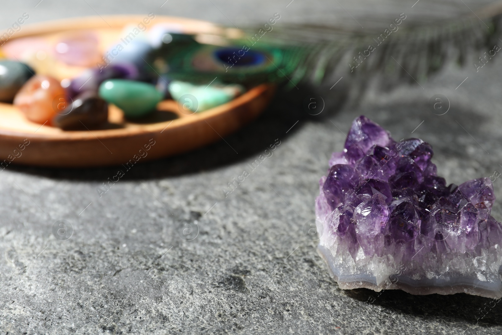 Photo of Beautiful gemstones and peacock feather on grey table, closeup