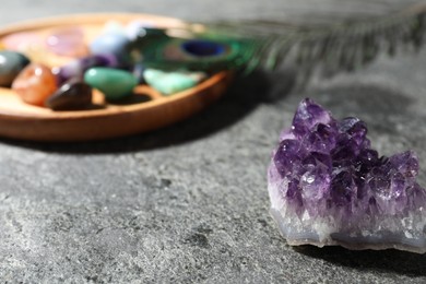 Photo of Beautiful gemstones and peacock feather on grey table, closeup
