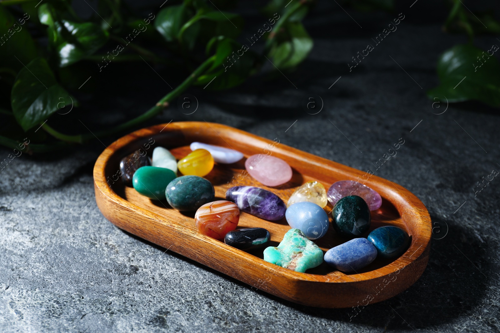 Different beautiful gemstones and green leaves on grey table, closeup Photo of Different beautiful gemstones and green leaves on grey table, closeup