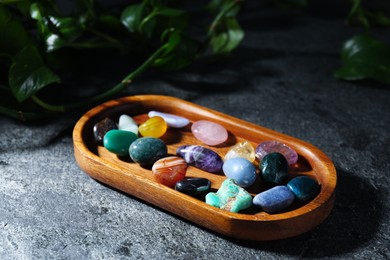 Photo of Different beautiful gemstones and green leaves on grey table, closeup