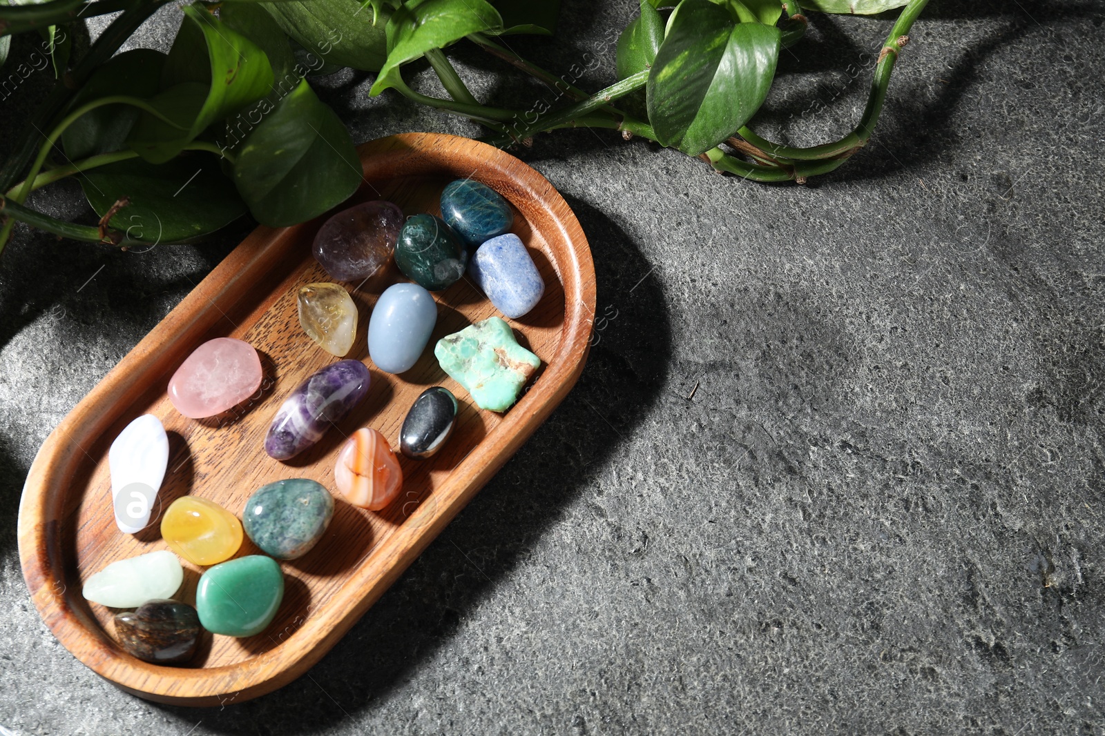 Photo of Different beautiful gemstones and green leaves on grey table, top view. Space for text
