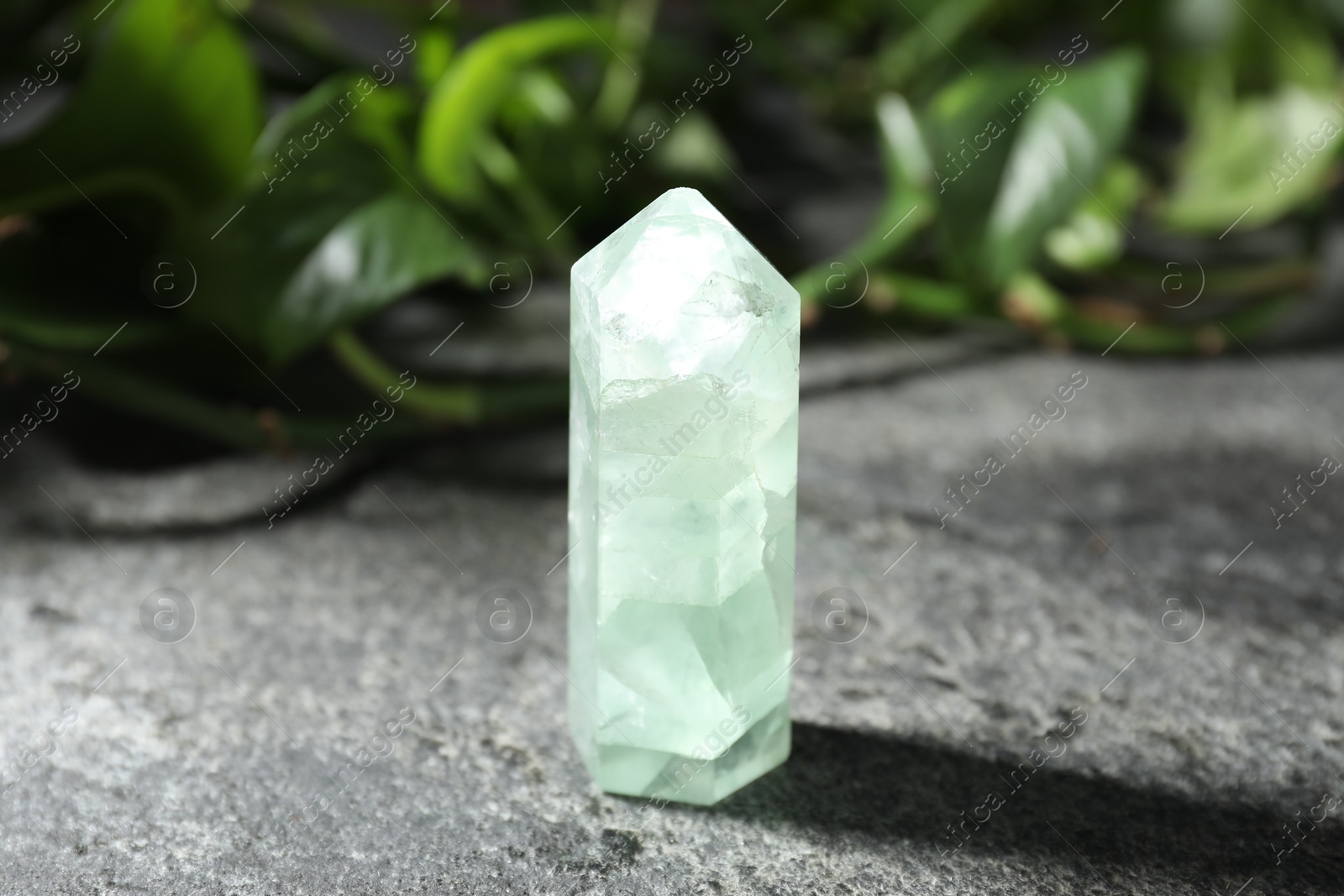 Beautiful fluorite gemstone and green leaves on grey table, closeup Photo of Beautiful fluorite gemstone and green leaves on grey table, closeup