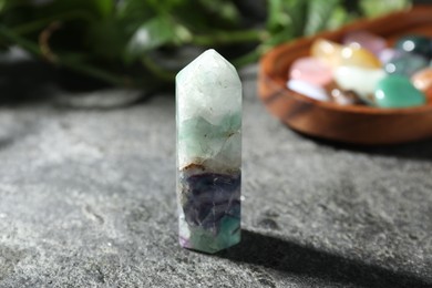 Photo of Beautiful fluorite gemstone, other mineral stones and green leaves on grey table, closeup