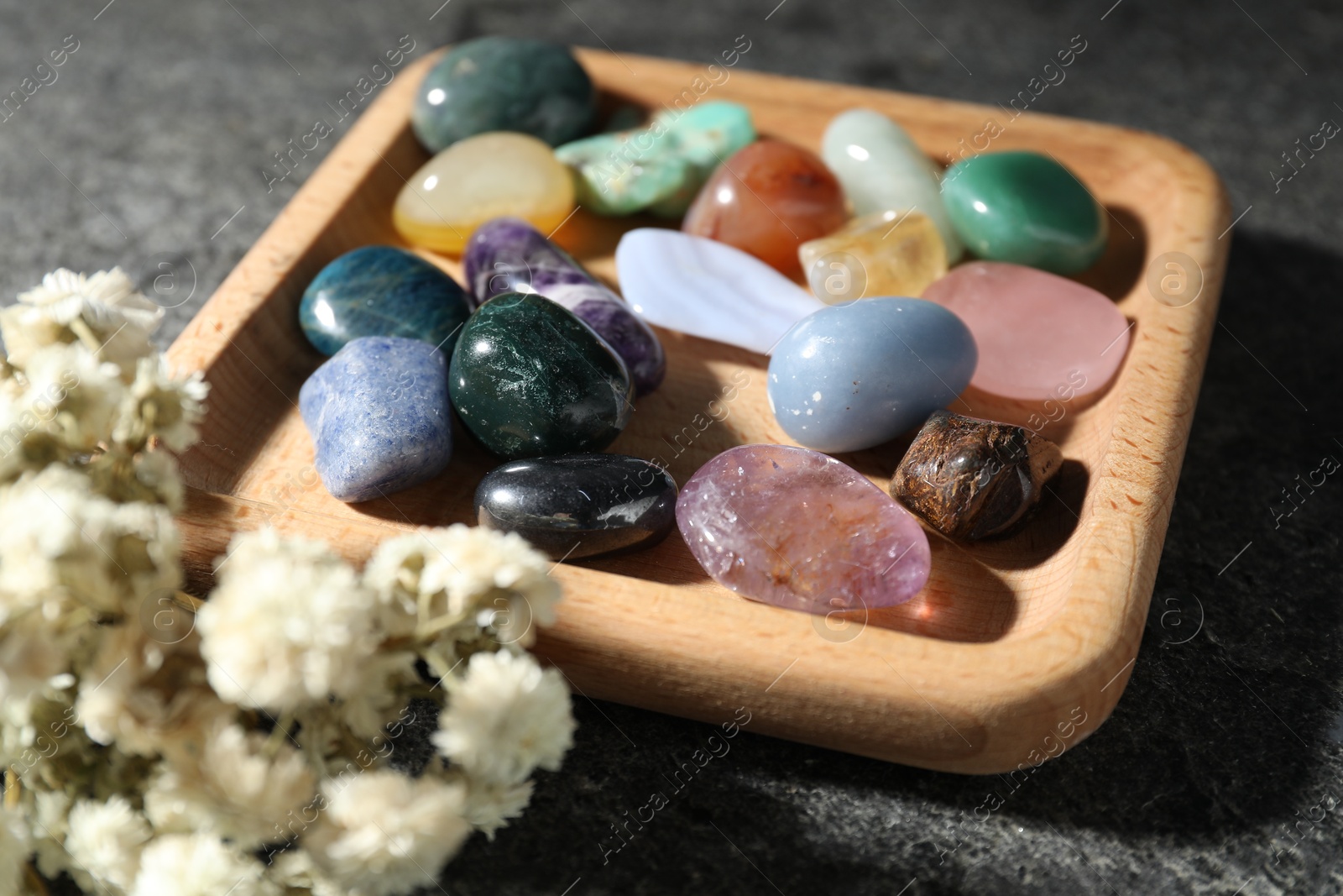 Photo of Different beautiful gemstones and dried flowers on grey table, closeup
