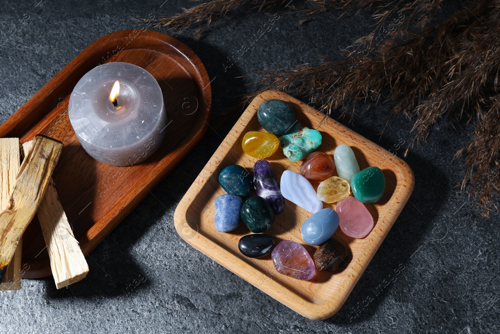 Photo of Different beautiful gemstones, palo santo, burning candle and dried reeds on grey table, flat lay