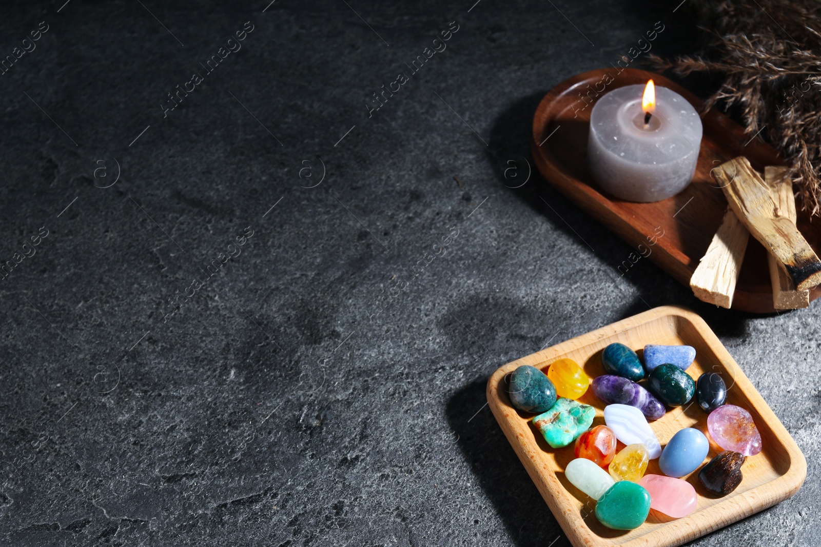 Photo of Different beautiful gemstones, palo santo, burning candle and dried reeds on grey table, closeup. Space for text