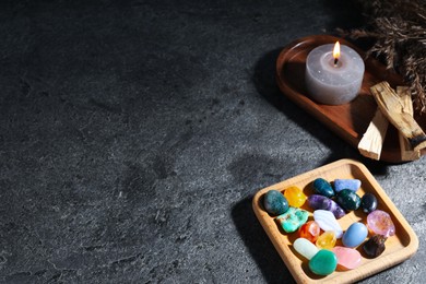 Photo of Different beautiful gemstones, palo santo, burning candle and dried reeds on grey table, closeup. Space for text