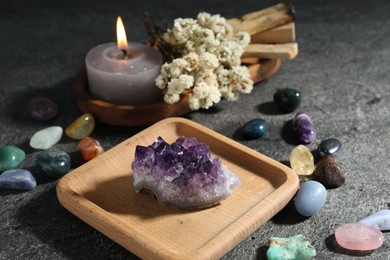 Photo of Different beautiful gemstones, palo santo, burning candle and dried flowers on grey table, closeup