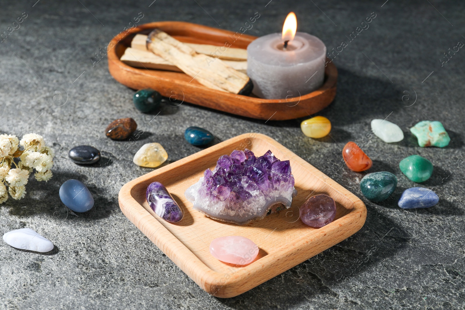 Photo of Different beautiful gemstones, palo santo, burning candle and dried flowers on grey table, closeup