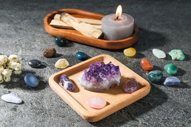 Photo of Different beautiful gemstones, palo santo, burning candle and dried flowers on grey table, closeup