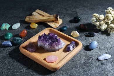 Photo of Different beautiful gemstones, palo santo and dried flowers on grey table, closeup