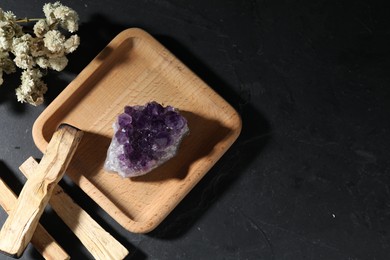 Photo of Beautiful amethyst gemstone, palo santo and dried flowers on black table, flat lay. Space for text