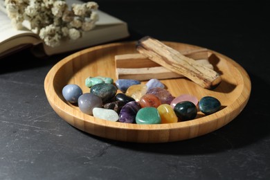 Photo of Different beautiful gemstones, palo santo, book and dried flowers on black table, closeup
