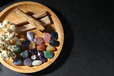 Photo of Different beautiful gemstones, palo santo and dried flowers on black table, top view. Space for text