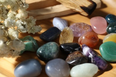 Photo of Different beautiful gemstones, palo santo and dried flowers on wooden plate, closeup