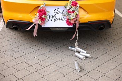 Photo of Wedding car. Cabriolet decorated with Just Married card, beautiful flowers and tin cans outdoors, closeup