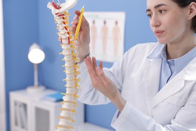 Photo of Doctor pointing at sections of human spine model in clinic
