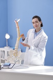 Photo of Doctor pointing at sections of human spine model at desk in clinic