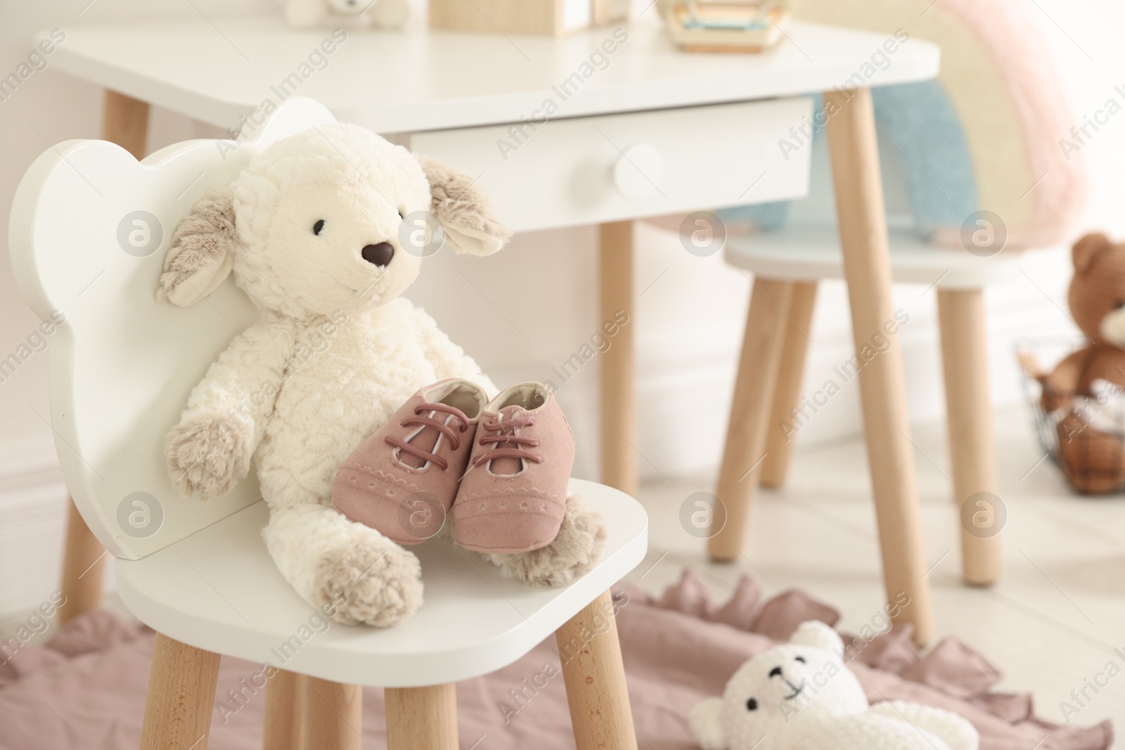 Photo of Cute soft toy sheep and baby shoes on chair indoors
