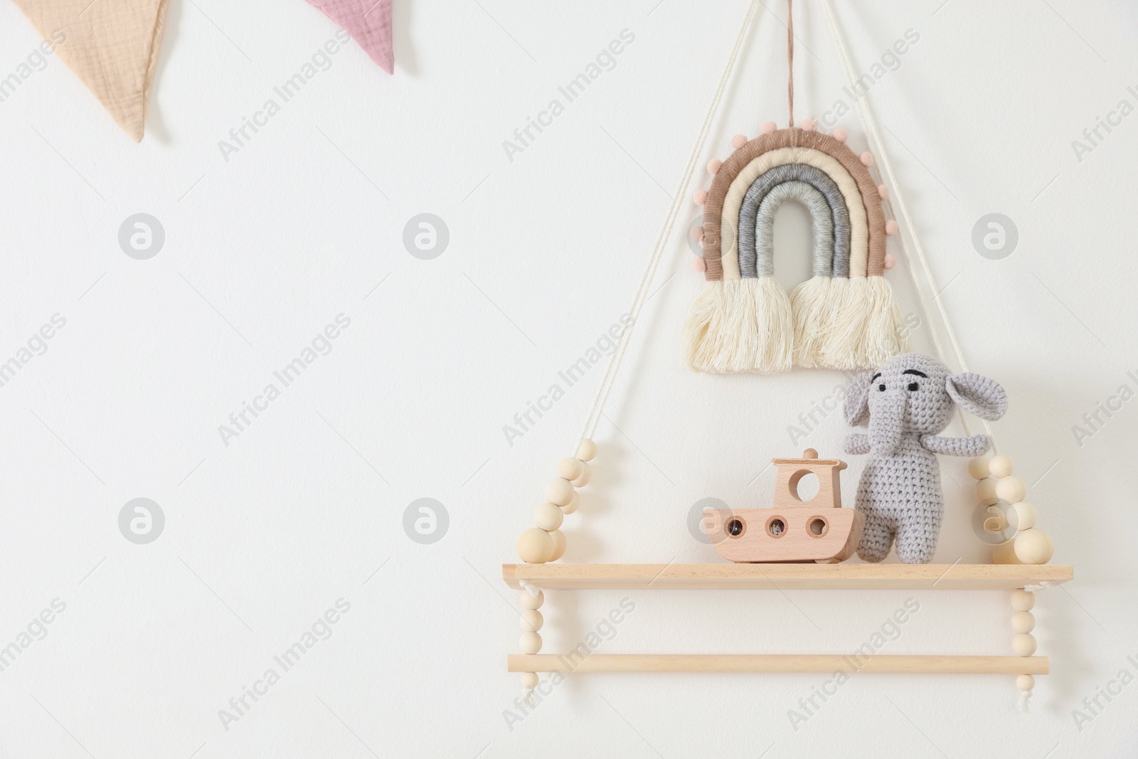 Photo of Shelf with soft toy elephant and wooden boat on white wall. Space for text