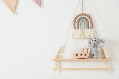 Photo of Shelf with soft toy elephant and wooden boat on white wall. Space for text