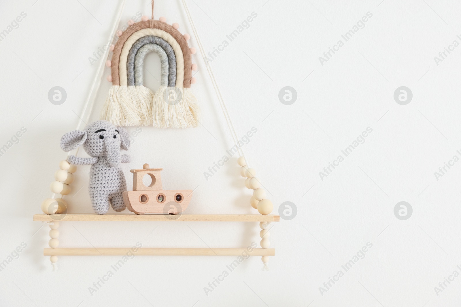 Photo of Shelf with soft toy elephant and wooden boat on white wall. Space for text