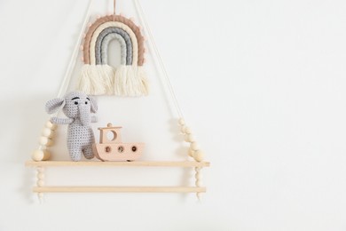 Photo of Shelf with soft toy elephant and wooden boat on white wall. Space for text