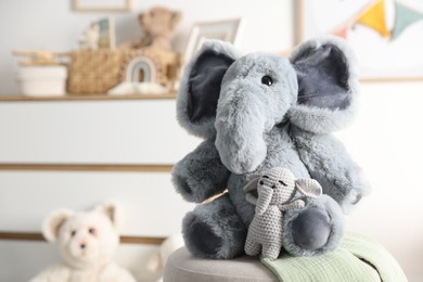 Photo of Cute soft toy elephants on pouf in child's room, closeup. Space for text