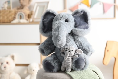 Photo of Cute soft toy elephants on pouf in child's room, closeup