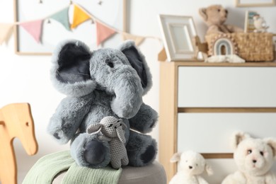 Photo of Cute soft toy elephants on pouf in child's room, closeup. Space for text