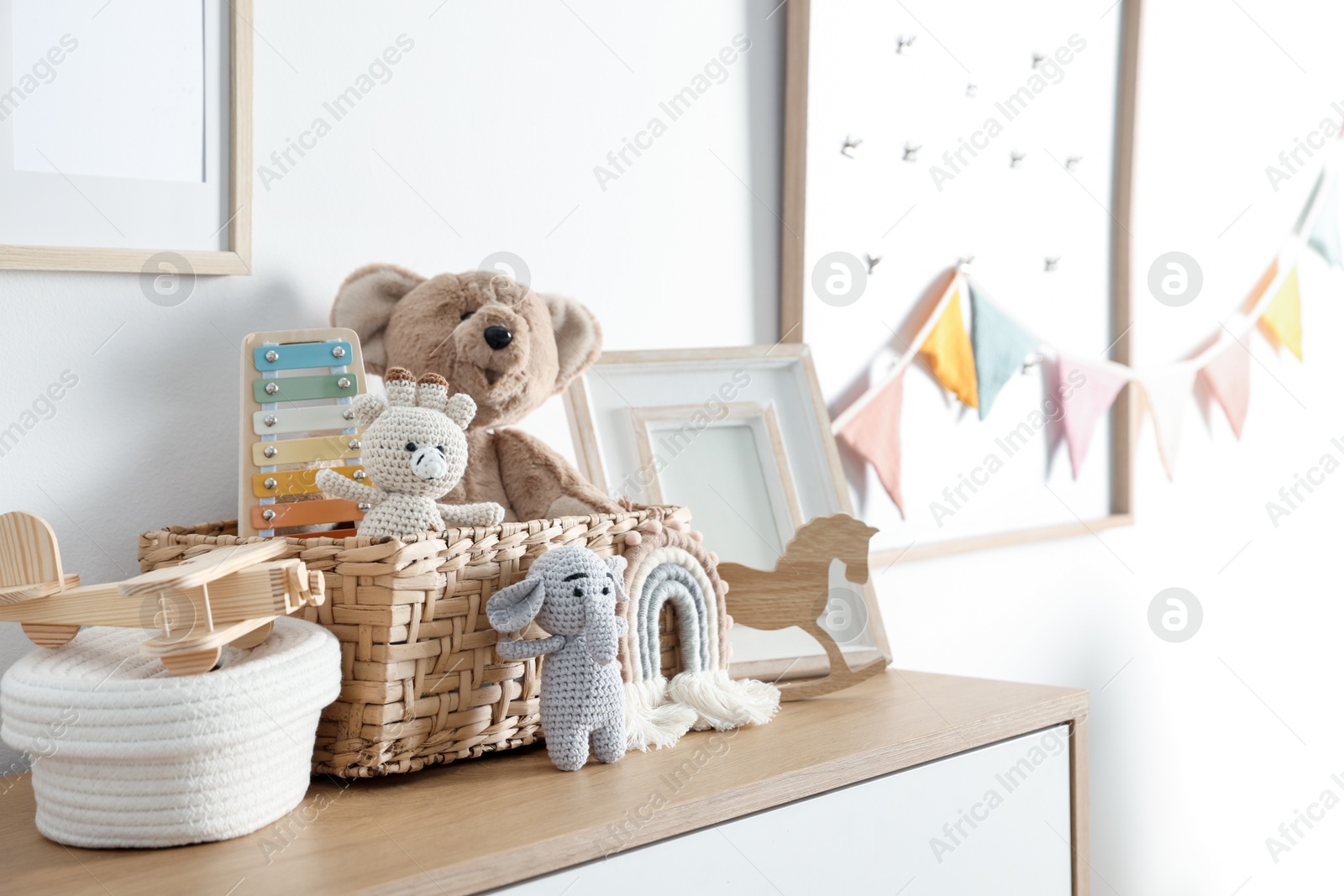 Photo of Different cute toys and decor on chest of drawers near white wall indoors