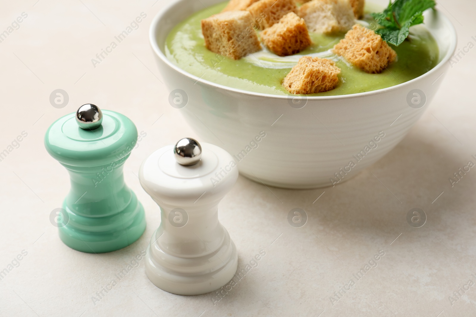 Photo of Salt and pepper mills near bowl of delicious cream soup with croutons on light table, closeup