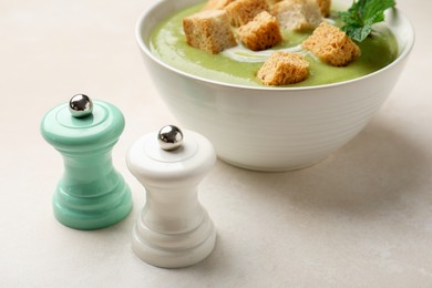 Photo of Salt and pepper mills near bowl of delicious cream soup with croutons on light table, closeup