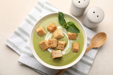 Photo of Salt and pepper shakers near bowl of delicious cream soup with croutons and mint on light table, flat lay