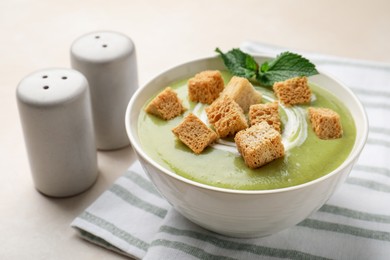Photo of Salt and pepper shakers near bowl of delicious cream soup with croutons on light table, closeup