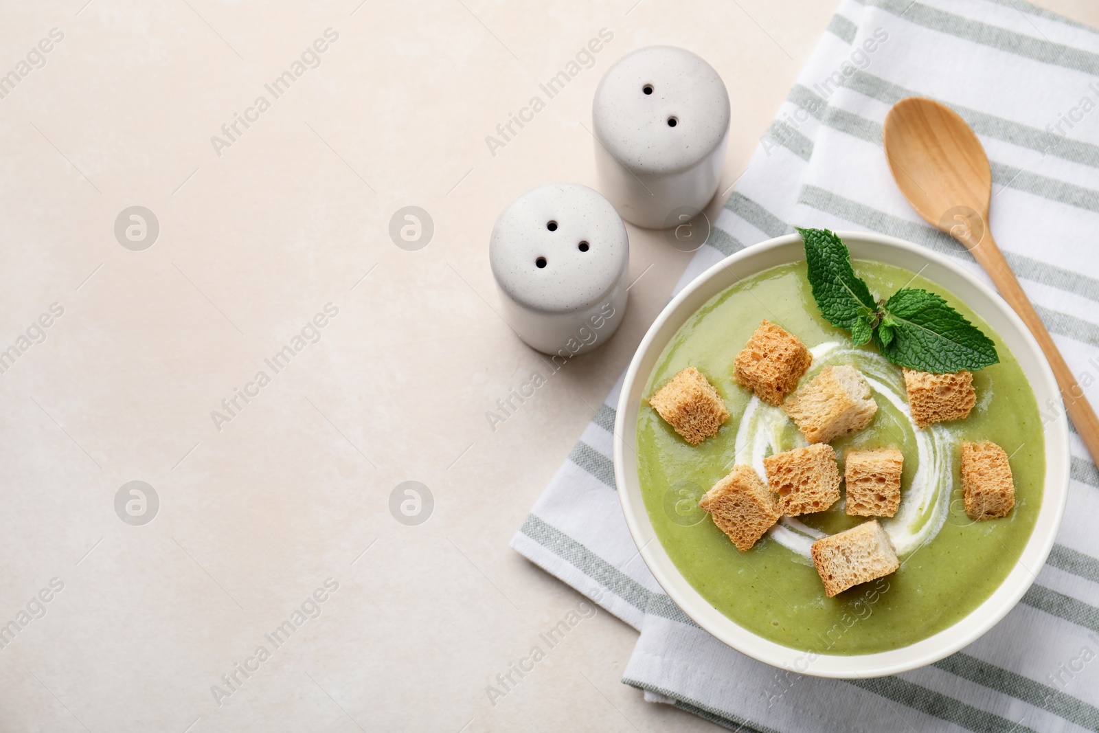 Photo of Salt and pepper shakers near bowl of delicious cream soup with croutons and mint on light table, flat lay. Space for text