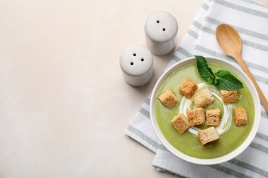 Photo of Salt and pepper shakers near bowl of delicious cream soup with croutons and mint on light table, flat lay. Space for text
