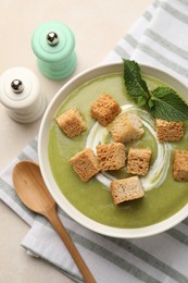 Photo of Salt and pepper mills near bowl of delicious cream soup with croutons and mint on light table, flat lay