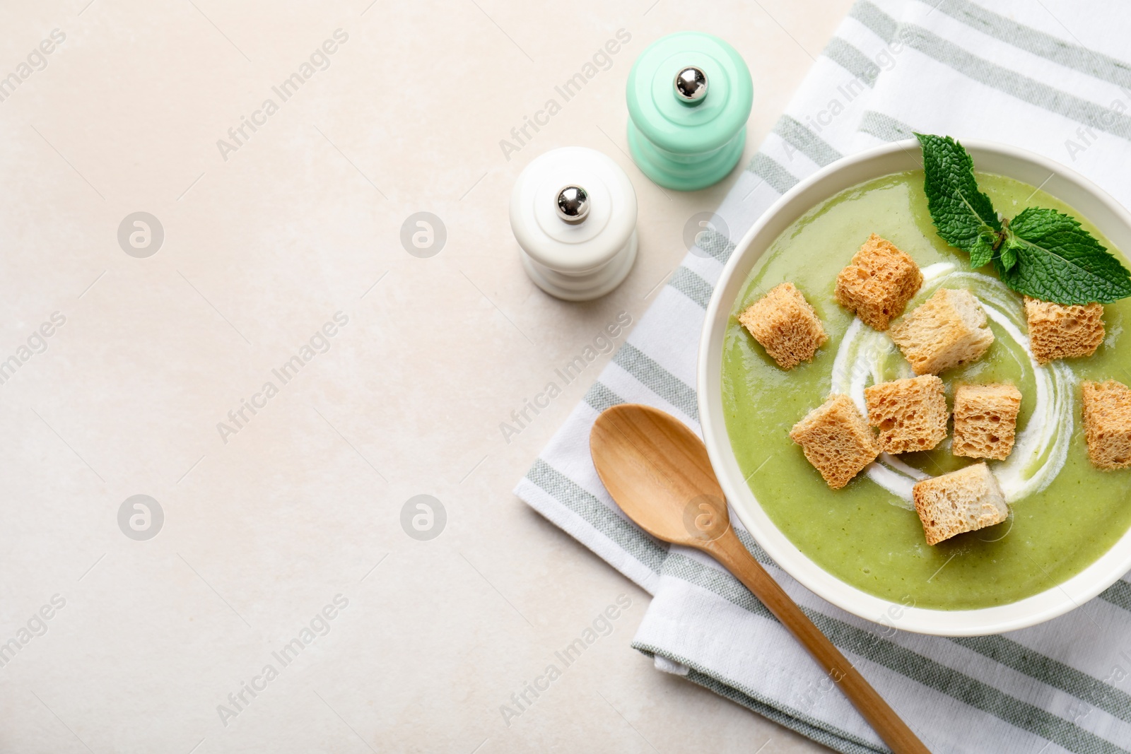 Photo of Salt and pepper mills near bowl of delicious cream soup with croutons and mint on light table, flat lay. Space for text