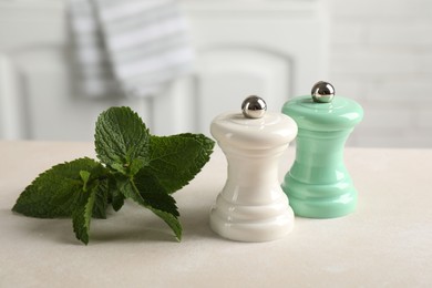 Photo of Salt, pepper mills and mint on light table indoors, closeup