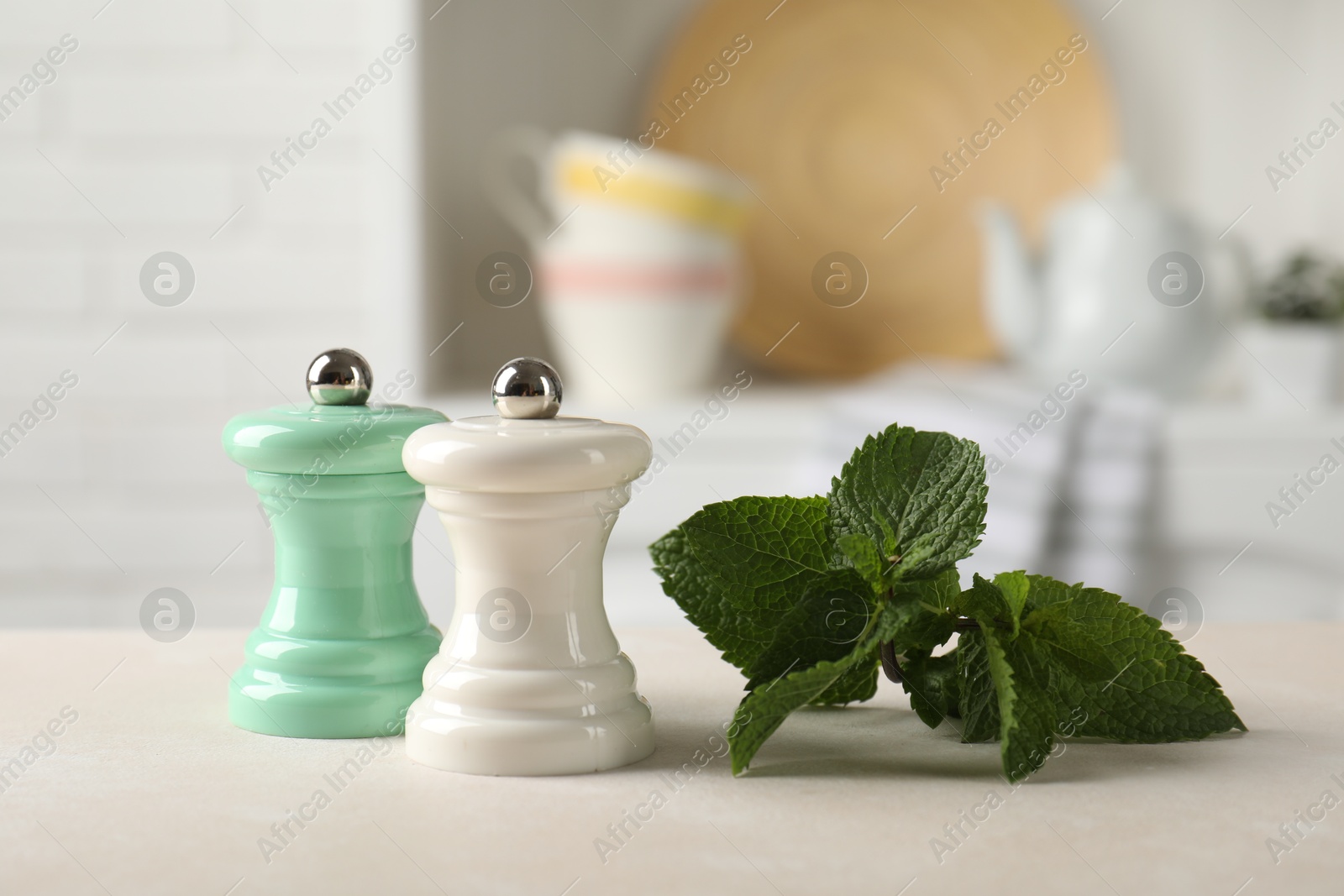Photo of Salt, pepper mills and mint on light table in kitchen, closeup