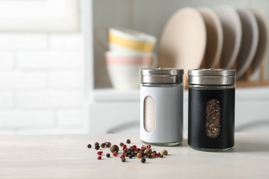 Photo of Salt, pepper shakers and peppercorns on light wooden table in kitchen, closeup. Space for text