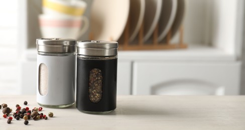 Photo of Salt, pepper shakers and peppercorns on light wooden table in kitchen, closeup. Space for text