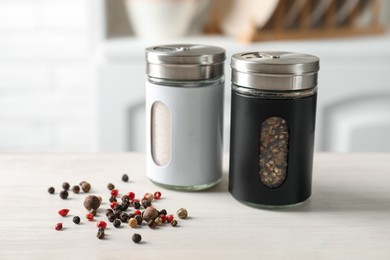 Photo of Salt, pepper shakers and peppercorns on light wooden table indoors, closeup