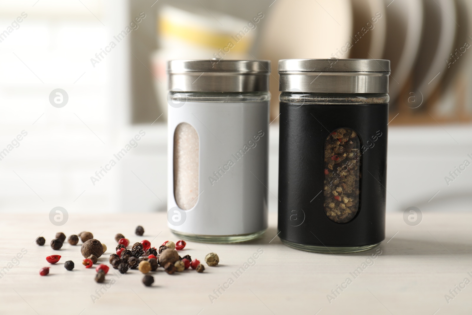 Photo of Salt, pepper shakers and peppercorns on light wooden table in kitchen, closeup