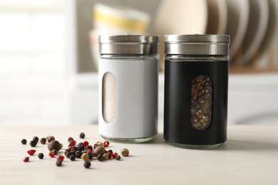 Photo of Salt, pepper shakers and peppercorns on light wooden table in kitchen, closeup
