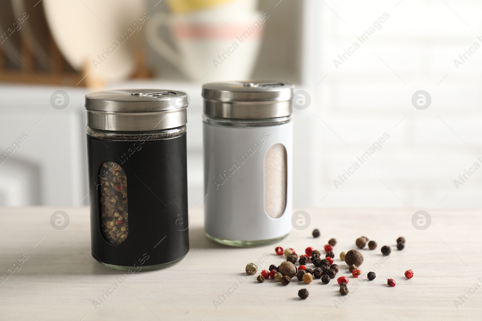 Photo of Salt, pepper shakers and peppercorns on light wooden table in kitchen, closeup