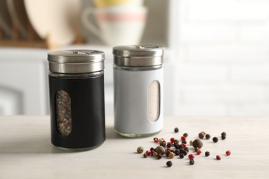 Photo of Salt, pepper shakers and peppercorns on light wooden table in kitchen, closeup