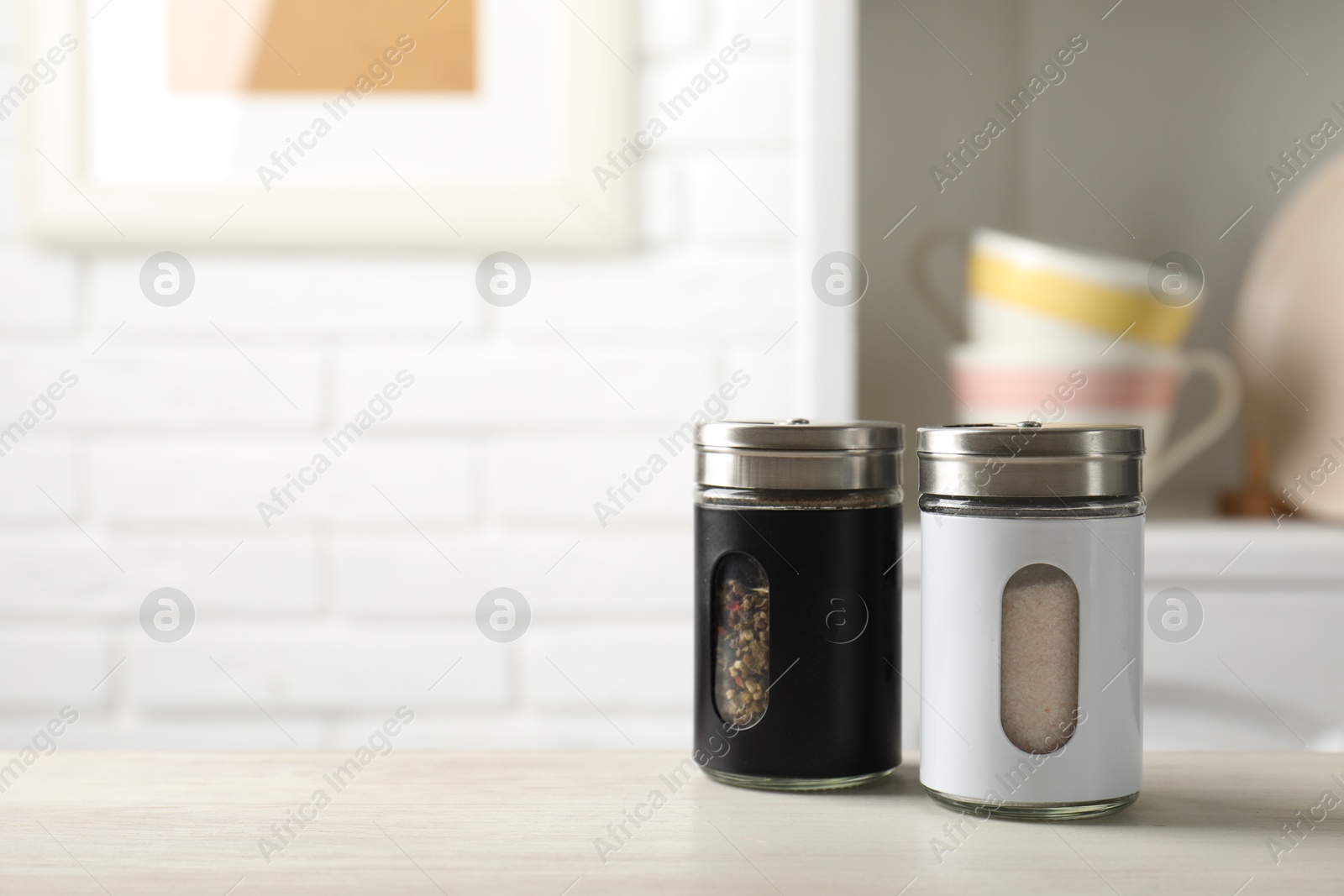 Photo of Salt and pepper shakers on light wooden table in kitchen, closeup. Space for text