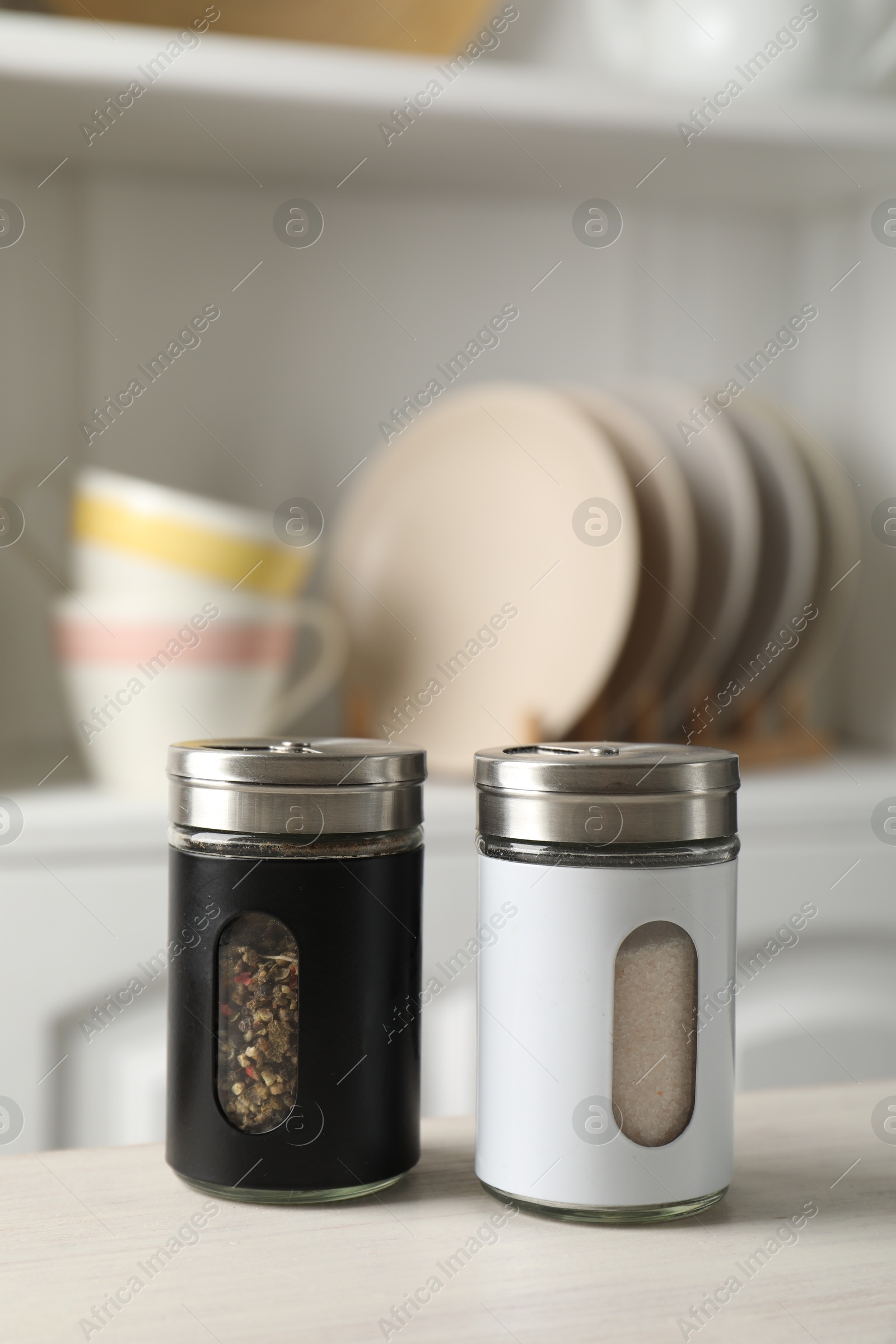 Photo of Salt and pepper shakers on light wooden table in kitchen, closeup. Space for text